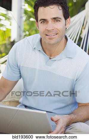 Stock Image - Mixed race man in hammock using laptop. Fotosearch