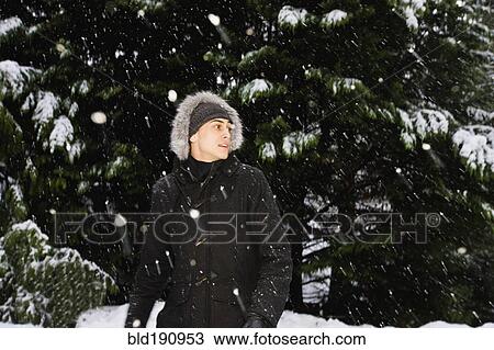 Stock Image - Mixed race man in hooded coat outdoors in snowfall. Fotosearch