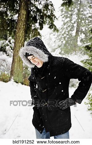 Stock Image - Mixed race man in hooded coat outdoors in snowfall. Fotosearch