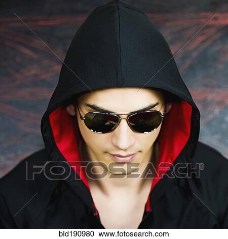Stock Image - Mixed race man in hooded jacket and sunglasses. Fotosearch