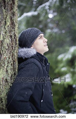 Stock Image - Mixed race man leaning against tree trunk. Fotosearch