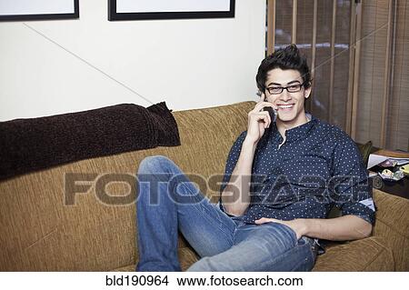 Mixed race man reclining on sofa talking on cell phone View Large Photo Image Picture - Mixed race man reclining on sofa talking on cell phone. Fotosearch