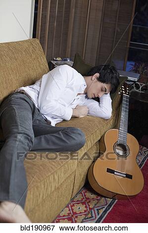 Mixed race man sleeping on sofa next to guitar View Large Photo Image Stock Photo - Mixed race man sleeping on sofa next to guitar. Fotosearch