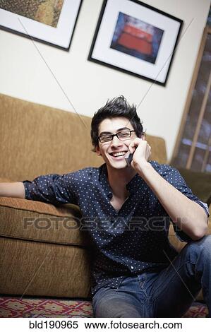 Stock Photography - Mixed race man talking on cell phone in living room. Fotosearch