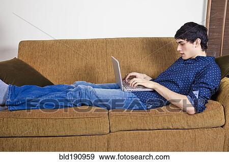 Stock Photo - Mixed race man typing on laptop on sofa. Fotosearch