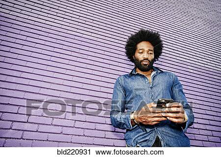 Stock Image - Mixed race man using cell phone outdoors. Fotosearch