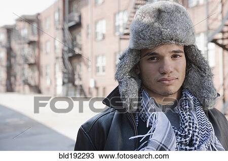 Stock Image - Mixed race man wearing fur hat on urban street. Fotosearch