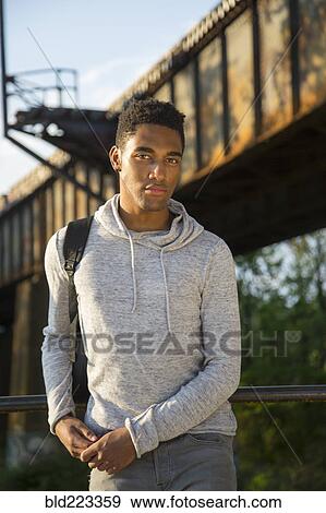 Stock Photo - Mixed Race man with backpack leaning on urban railing. Fotosearch