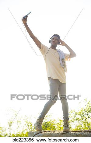 Mixed Race man with shirt draped over shoulders listening to headphones View Large Photo Image Stock Photograph - Mixed Race man with shirt draped over shoulders listening to headphones. Fotosearch