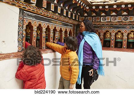 Stock Image - Mixed Race mother and sons spinning prayer wheels. Fotosearch