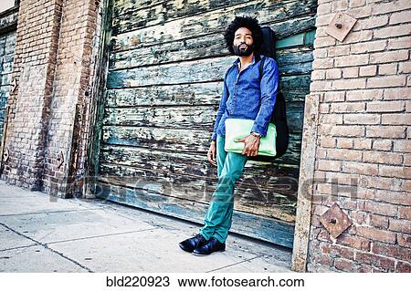 Stock Image - Mixed race musician carrying laptop outdoors. Fotosearch