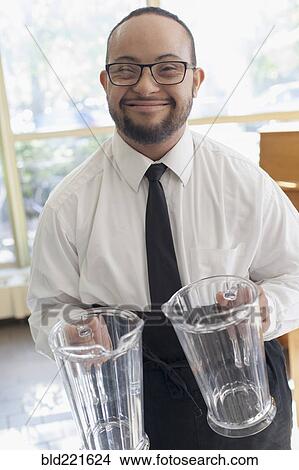 Mixed race server with down syndrome holding pitchers in restaurant View Large Photo Image Picture - Mixed race server with down syndrome holding pitchers in restaurant. Fotosearch