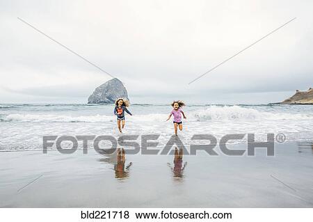 Stock Photo - Mixed race sisters running on beach. Fotosearch