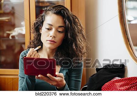 Stock Photograph - Mixed race woman applying makeup in mirror. Fotosearch