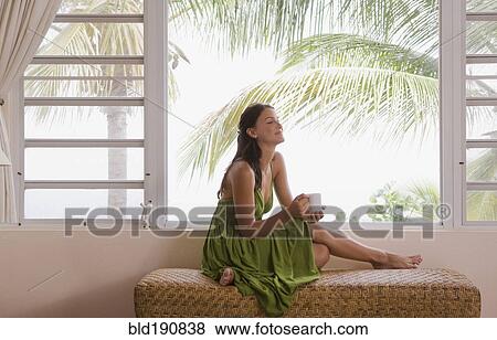 Mixed race woman drinking coffee near window View Large Photo Image Stock Photo - Mixed race woman drinking coffee near window. Fotosearch