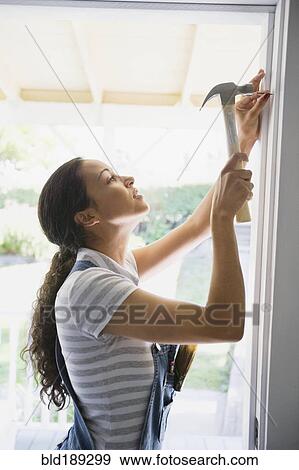 Mixed race woman hammering nail in doorway View Large Photo Image Stock Photo - Mixed race woman hammering nail in doorway. Fotosearch
