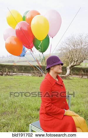 Stock Image - Mixed race woman holding colorful bunch of balloons. Fotosearch