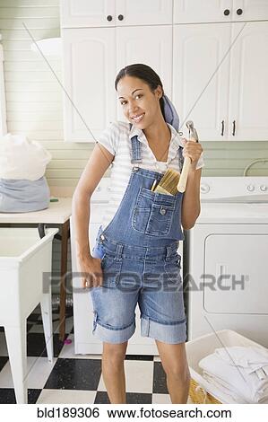 Stock Photograph - Mixed race woman holding hammer in laundry room. Fotosearch