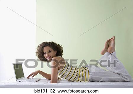 Stock Image - Mixed race woman laying on sofa using laptop. Fotosearch