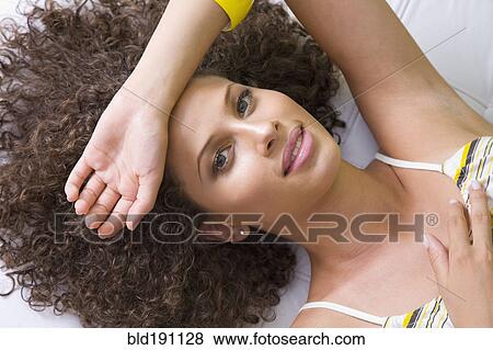 Stock Photo - Mixed race woman laying with arm over forehead. Fotosearch
