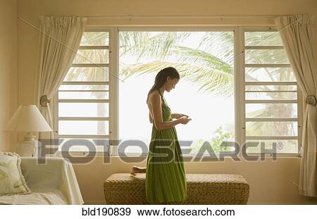 Stock Photo - Mixed race woman looking at cell phone near window. Fotosearch
