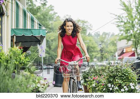 Stock Image - Mixed race woman riding bicycle in city. Fotosearch