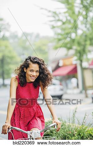Stock Photo - Mixed race woman riding bicycle in city. Fotosearch