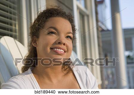 Stock Image - Mixed race woman sitting on porch. Fotosearch