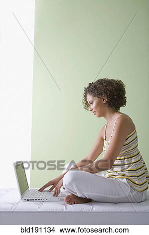 Picture - Mixed race woman sitting on sofa using laptop. Fotosearch