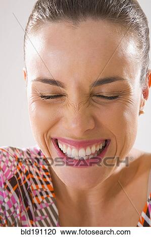 Stock Image - Mixed race woman smiling and grimacing with eyes closed. Fotosearch