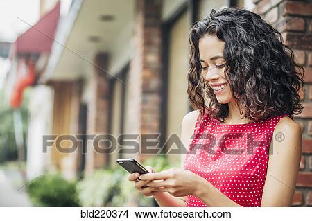 Picture - Mixed race woman using cell phone in city. Fotosearch