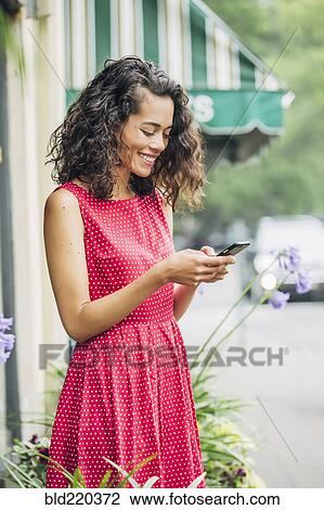 Stock Image - Mixed race woman using cell phone in city. Fotosearch
