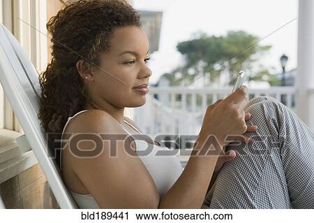 Stock Image - Mixed race woman using cell phone on porch. Fotosearch