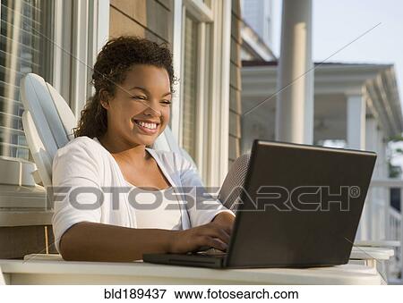Stock Photo - Mixed race woman using laptop on porch. Fotosearch