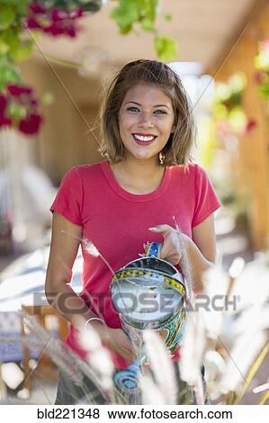 Stock Photo - Mixed race woman watering plants in garden. Fotosearch