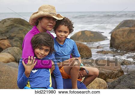 Stock Image - Mother and children hugging on rocky beach. Fotosearch