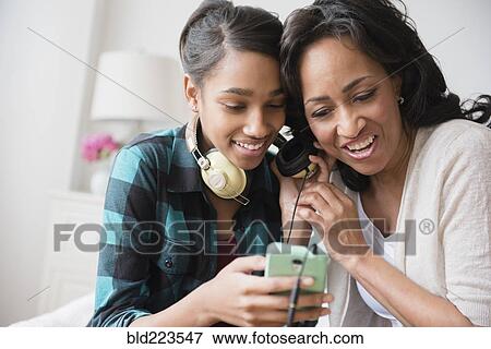 Mother and daughter listening to cell phone music on headphones View Large Photo Image Stock Photo - Mother and daughter listening to cell phone music on headphones. Fotosearch