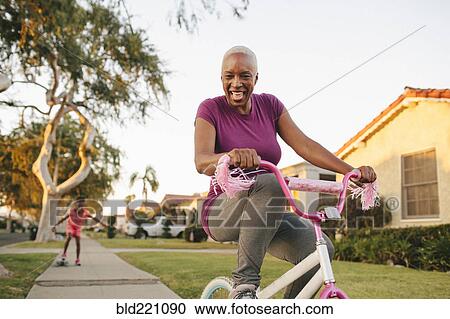Stock Image - Mother and daughter riding skateboard and bicycle. Fotosearch