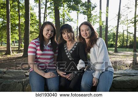 Stock Image - Mother and mixed race daughters sitting on stone wall. Fotosearch
