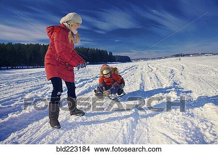 Mother and sons sledding in snowy remote field View Large Photo Image Picture - Mother and sons sledding in snowy remote field. Fotosearch