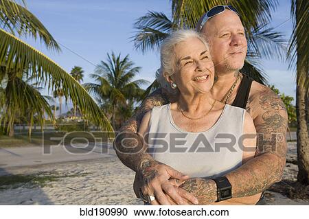 Stock Image - Mother and tattooed son hugging at the beach. Fotosearch