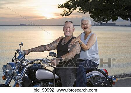 Stock Image - Mother and tattooed son riding motorcycle at the beach. Fotosearch