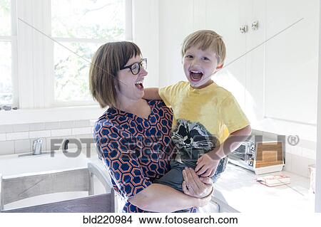 Picture - Mother holding son in kitchen. Fotosearch