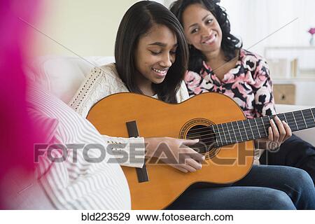 Mother watching daughter play guitar on sofa View Large Photo Image Stock Photo - Mother watching daughter play guitar on sofa. Fotosearch