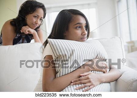Stock Photography - Mother watching pensive daughter clutching pillow. Fotosearch