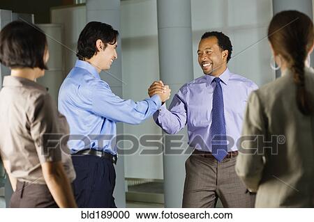 Stock Image - Multi-ethnic co-workers shaking hands in office. Fotosearch