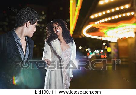 Stock Image - Multi-ethnic couple holding hands and laughing outside nightclub. Fotosearch