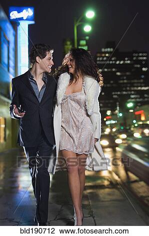 Stock Image - Multi-ethnic couple in formal attire walking down sidewalk. Fotosearch