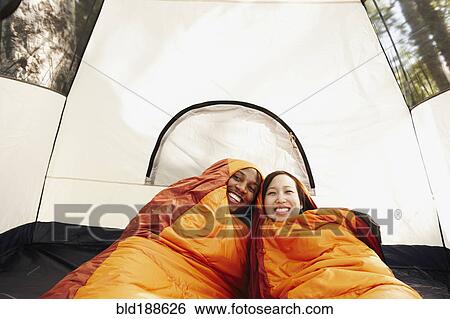 Stock Photograph - Multi-ethnic couple inside sleeping bags and tent. Fotosearch