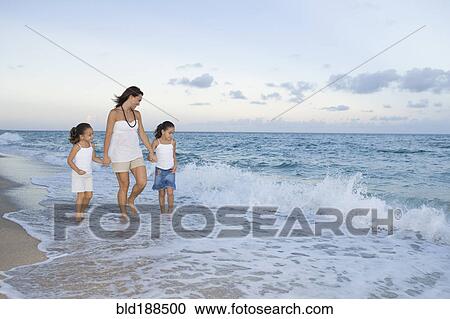 Stock Image - Multi-ethnic mother and daughters walking through ocean surf. Fotosearch